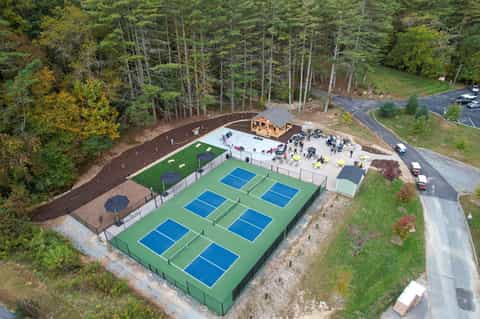 Aerial view of pickleball courts with green playing surfaces surrounded by forest