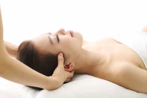 Woman receiving head massage in spa treatment room with white linens