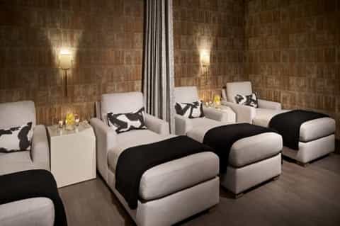 Spa relaxation room with multiple massage beds, cream upholstery, and ambient stone wall lighting