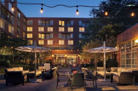Illuminated courtyard patio at dusk with seating areas, string lights, and brick building backdrop