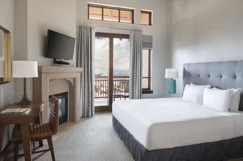 Upscale hotel bedroom with fireplace, balcony access, flatscreen TV, and mountain views