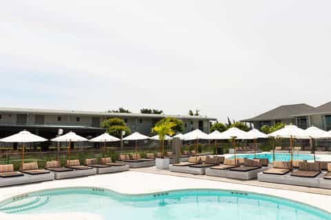 Resort pool deck with white umbrellas, striped lounge chairs, and calm turquoise water