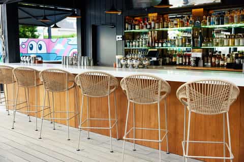 Modern beachfront bar with white woven stools, extensive liquor shelves, and colorful artwork