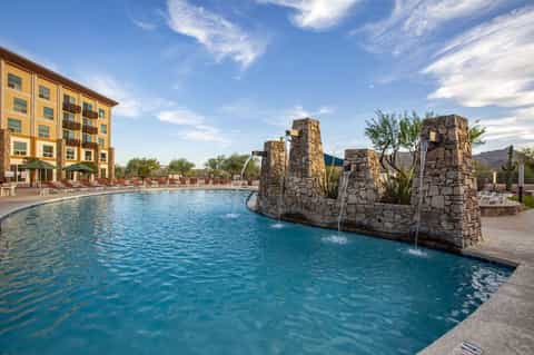 Resort pool with stone water features, loungers, yellow hotel building, and mountain landscape backdrop