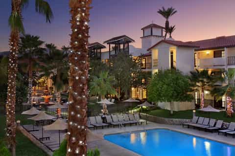 Luxury resort courtyard at dusk with illuminated palms, pool, and architecture