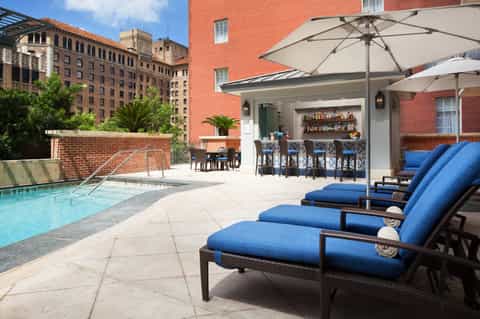 Urban rooftop pool with lounge chairs, bar area, umbrellas, and surrounding brick buildings