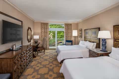 Upscale hotel room with two queen beds, flat-screen TV, balcony view, and traditional wood furnishings