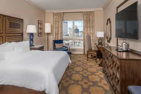 Upscale hotel bedroom with white bedding, city view windows, and elegant furnishings