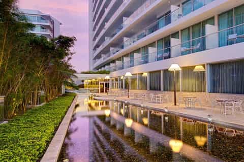 Modern residential building at dusk with reflection pool, landscaping, and lit ground-floor amenities