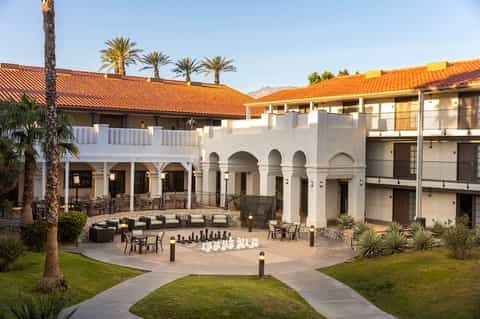 Mediterranean-style courtyard with white columns, arched doorways, palm trees, and giant chessboard