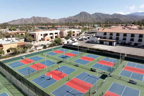 Multiple tennis courts with blue and red playing surfaces in desert setting