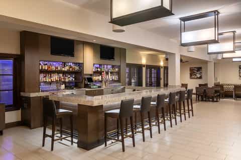 Upscale hotel bar lounge with granite countertop, illuminated bottle display, and bar seating