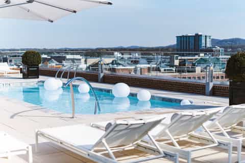 Rooftop pool with white loungers, umbrellas, and cityscape in background