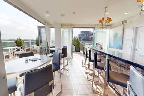Upscale rooftop dining space with floor-to-ceiling windows, modern furniture, and city skyline view