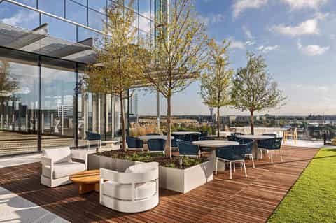 Rooftop terrace with modern lounge seating, trees, and panoramic city skyline views