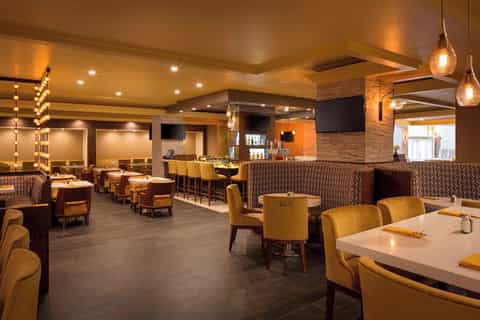 Upscale restaurant lounge with warm lighting, brick walls, pendant lights, gold chairs, and bar seating