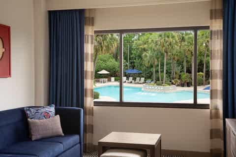 Hotel room interior with blue sofa overlooking large windows framing the resort pool area