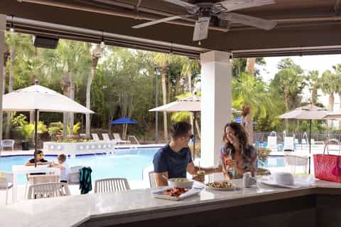 Poolside dining area under covered pavilion with guests and tropical views