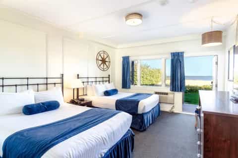 Oceanview hotel room with four beds, metal headboards, blue accents, windows overlooking beach and ocean