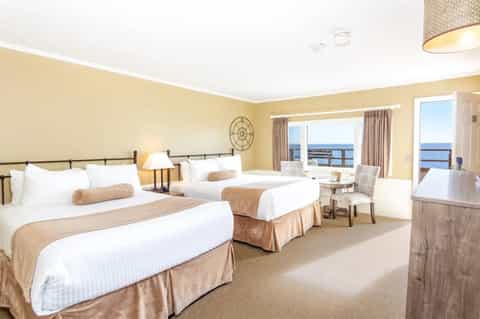 Oceanview hotel room with two beds, neutral bedding, and panoramic water views from balcony