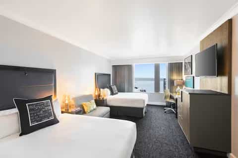 Upscale hotel bedroom with two beds, ocean view windows, modern furnishings, and flat-screen TV