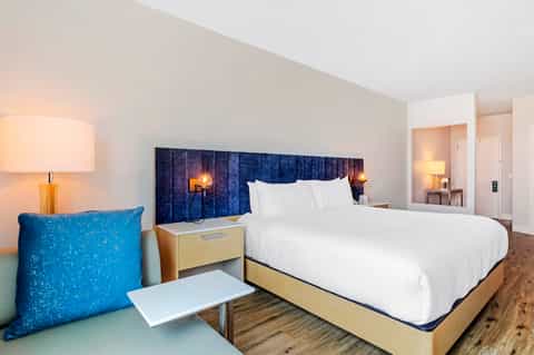 Contemporary hotel bedroom with blue headboard, white linens, wooden nightstands, and warm lighting