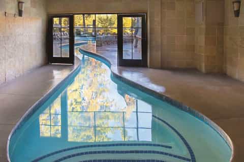 Indoor lazy river flowing through stone-tiled corridor with glass doors opening to outdoor pool