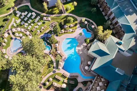 Aerial view of large resort with multiple shaped pools, landscaped grounds, and waterfront location