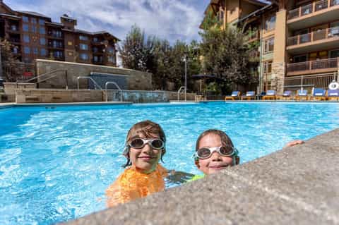 Two children swimming in bright blue resort pool wearing goggles
