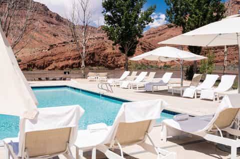Resort pool deck with white loungers, umbrellas, and mountain backdrop
