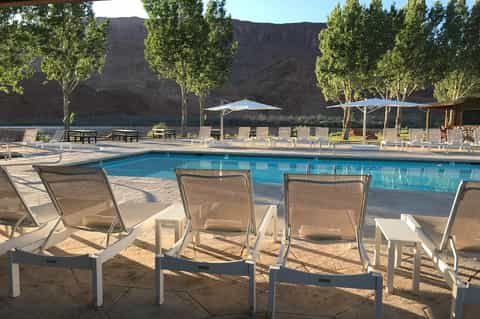 Resort pool with lounge chairs, umbrellas, and dramatic canyon rock formations in background