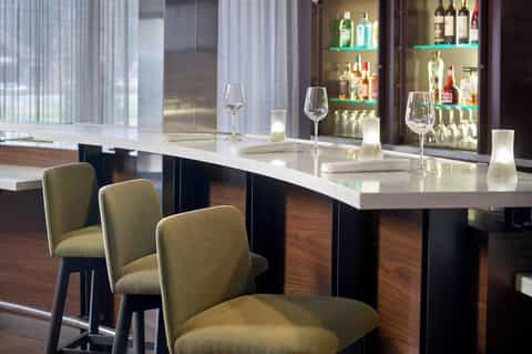 Upscale bar counter with white marble top, bar seating, and illuminated liquor shelves with modern styling