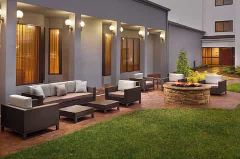 Modern courtyard with rattan furniture, fire pit, lit windows, and manicured lawn at evening