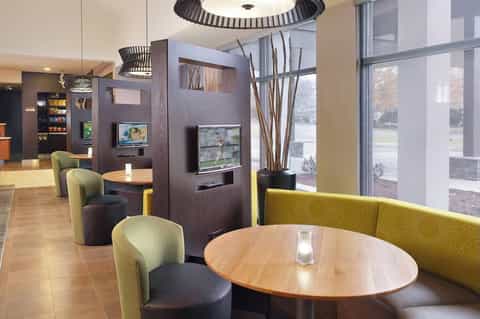 Modern hotel lobby lounge with contemporary furniture, decorative panels, TV screens, and large windows