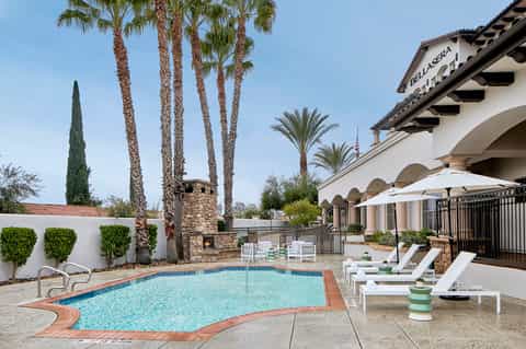 Resort pool area with pale blue water, white loungers, palm trees, and Spanish colonial architecture