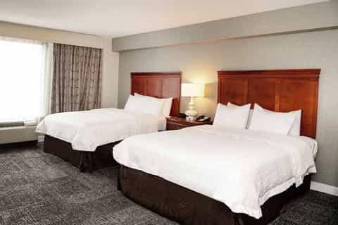 Hotel room with two queen beds, burgundy headboards, beige wallpaper, and traditional furnishings