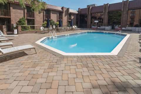 Resort pool with brick buildings, loungers, umbrellas, fencing, and patio area in sunny weather