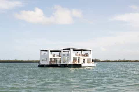 Modern white houseboat structure floating on calm turquoise water in nature