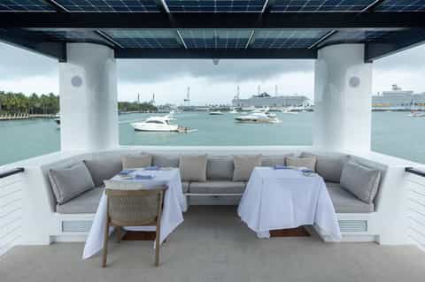 Luxury yacht dining area with gray seating, white tablecloths, and view of boats and marina