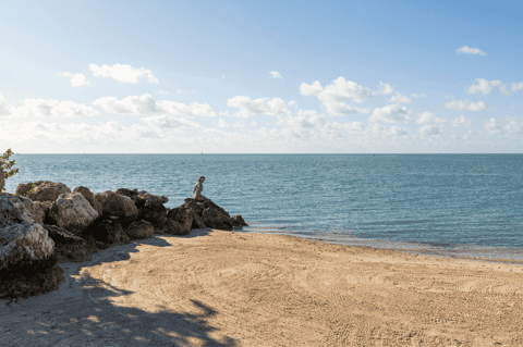 Serene rocky beach cove with calm turquoise water, sandy shore, and person on rock formations