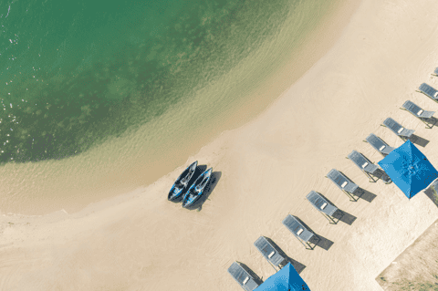 Aerial view of pristine beach with kayaks, lounge chairs, blue umbrellas and turquoise water