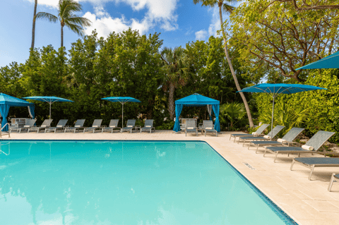 Turquoise pool with lounge chairs under blue umbrellas surrounded by lush tropical landscaping