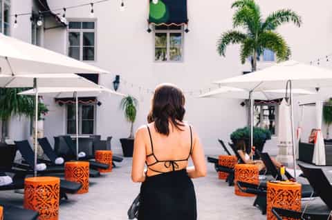Woman walking through courtyard with white umbrellas, black lounge chairs, and orange decorative planters
