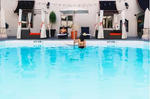 Resort pool with cabanas featuring white drapes, red accents, and poolside lounge seating