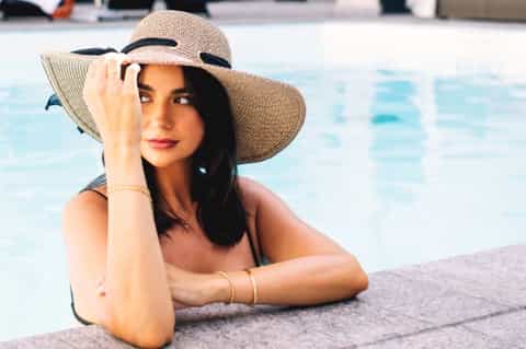 Woman in wide-brimmed hat relaxing poolside by turquoise water