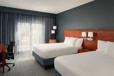 Hotel guest room with two queen beds, teal accent wall, and oceanview balcony doors
