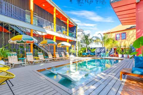 Vibrant resort pool area with colorful umbrellas, multi-story building, and tropical landscaping