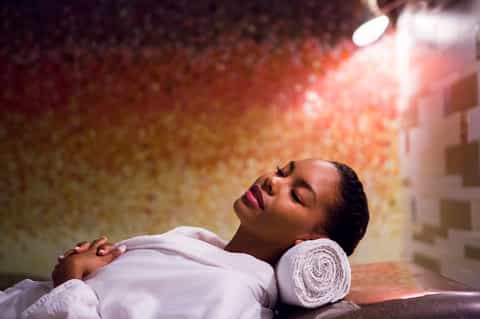 Woman receiving spa massage treatment with rolled towel pillow on terracotta stone backdrop