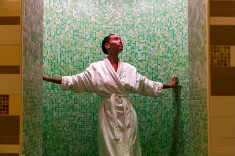 Woman in white robe relaxing in spa steam room with green mosaic tile walls