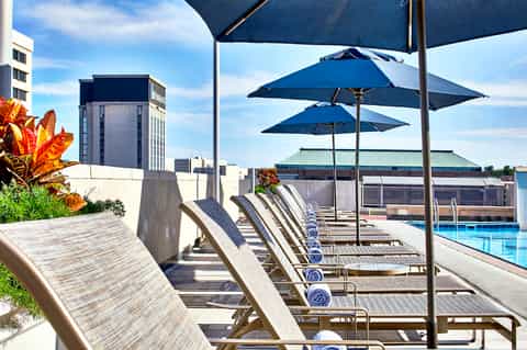Rooftop pool deck with blue umbrellas, lounge chairs, and urban skyline background